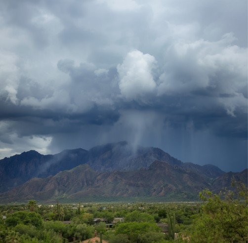 Heavy monsoon clouds descending from the mountains into Tucson, the sky thick with storm and desert light.